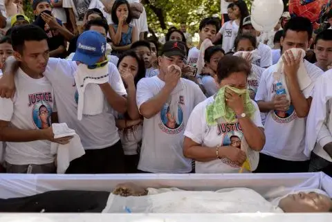 A family and friends of the deceased grieve standing before an open casket.