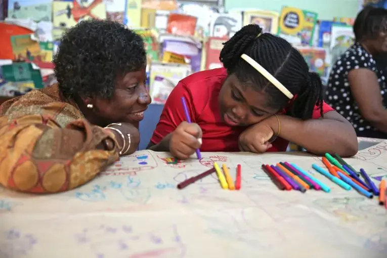 Dr. Claudette Crawford-Brown interacts with Shaniqua Long during an art therapy session at Shortwood Practising Infant, Primary and Junior High School in Kingston, Jamaica. Long's mother migrated to the United States. Image by Sabriya Simon. Jamaica.