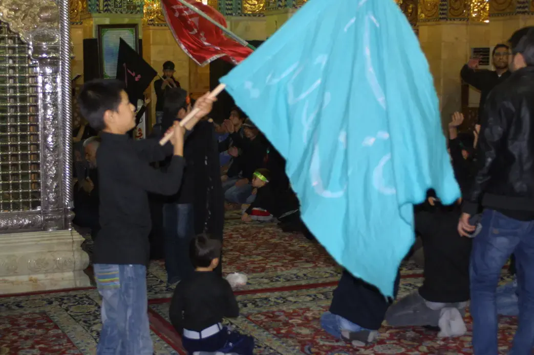 Young Syrian in Damascus waves a flag in support of the Syrian government of Bashar al Assad. Image by Reese Erlich. Syria 2013. Media file: rukaya_shrine_2.jpg