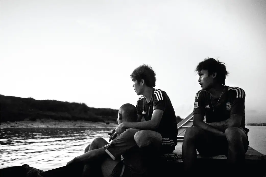 Arkar Min, a former child soldier, works on the Yangon River for a fisherman who is a big fan of the Chelsea soccer club and makes his employees wear the team's jersey as a uniform. Image by Spike Johnson. Burma, 2014. Media file: on-a-boat.jpg