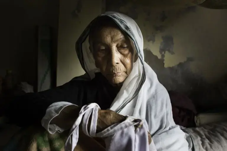 An elderly widow in her bed at Tarash Mandir, a short-stay home for young women and permanent facility for elderly widows in Vrindavan, India. This is the first and oldest home for widows in Vrindavan. Image by Amy Toensing. India, 2016.