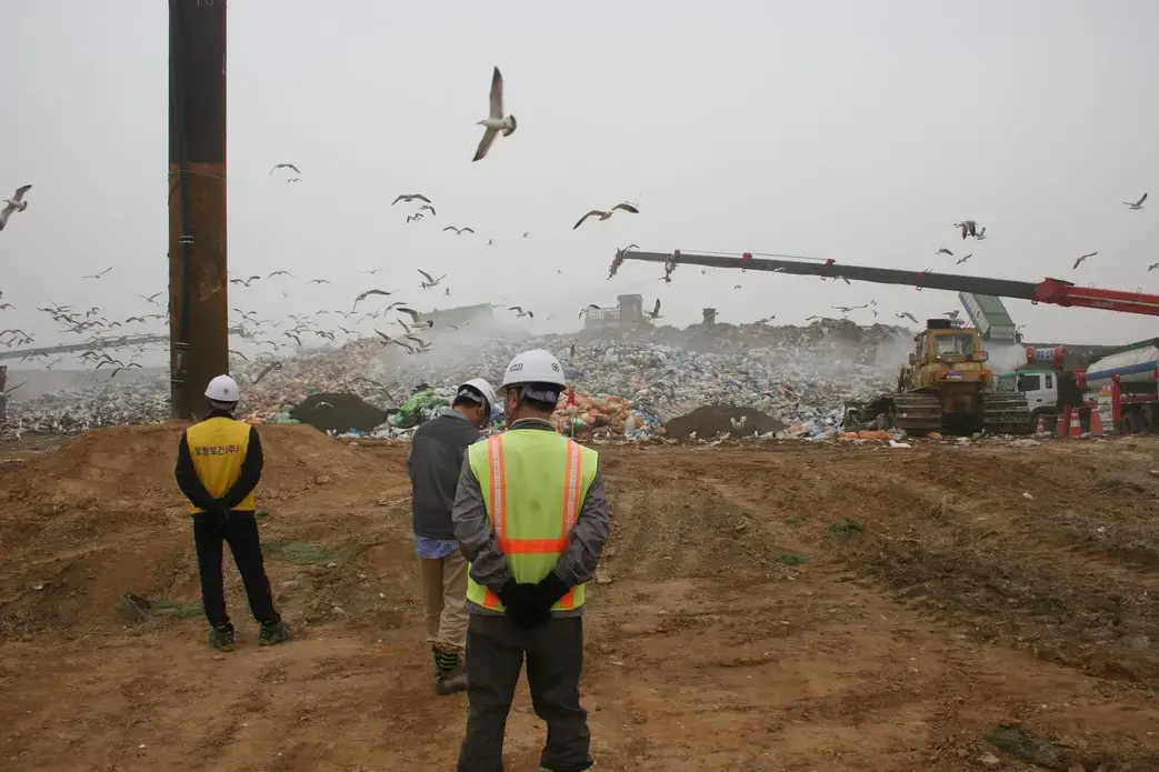 Landfill workers look onto mountains of garbage. About 360 tons of waste are collected at this landfill every day. The landfill operator has managed to turn garbage into a profitable business by harvesting methane from waste. It is then turned into electricity and sold to local power plants. The landfill is completely food waste free. Image by Karim Chrobog. South Korea, 2014. Media file: unnamed-6.jpg
