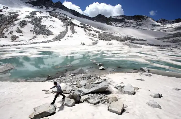 A man walks over rocks near to a glacial lake that has formed at the base of the Dagu Glacier on the southeast edge of the Tibetan Plateau. The glacier has been reducing in size in recent years as a result of rising temperatures in the region. Image by Sean Gallagher. China, 2012. Media file: meltdown_gallagher_1.jpg