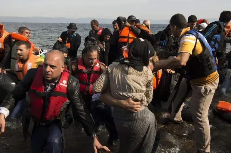 Refugees climb out of their dinghy on the shores of Lesbos after having crossed from Turkey, about seven miles away. Image by Tzeli Hadjidimitiou. Greece, 2015.