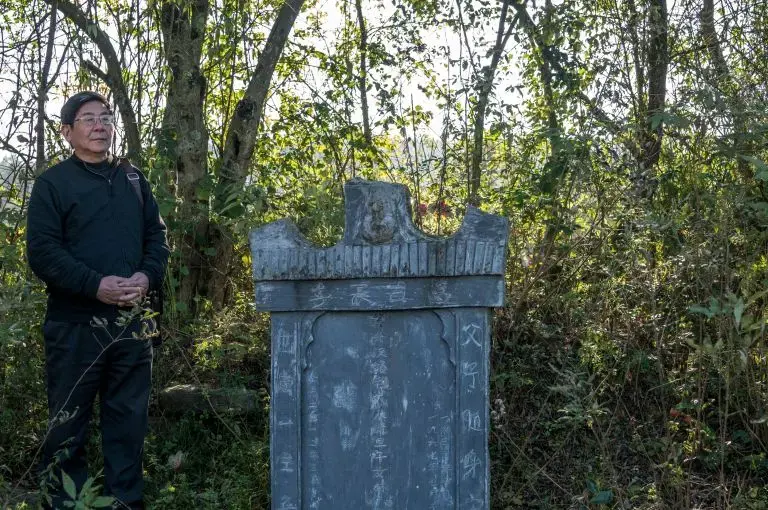 Tan Hecheng at a tombstone put up by Zhou Qun for her husband and three children, who were among the thousands of people killed during the Cultural Revolution in Dao County. Image by Sim Chi Yin. China/VII, 2016.
