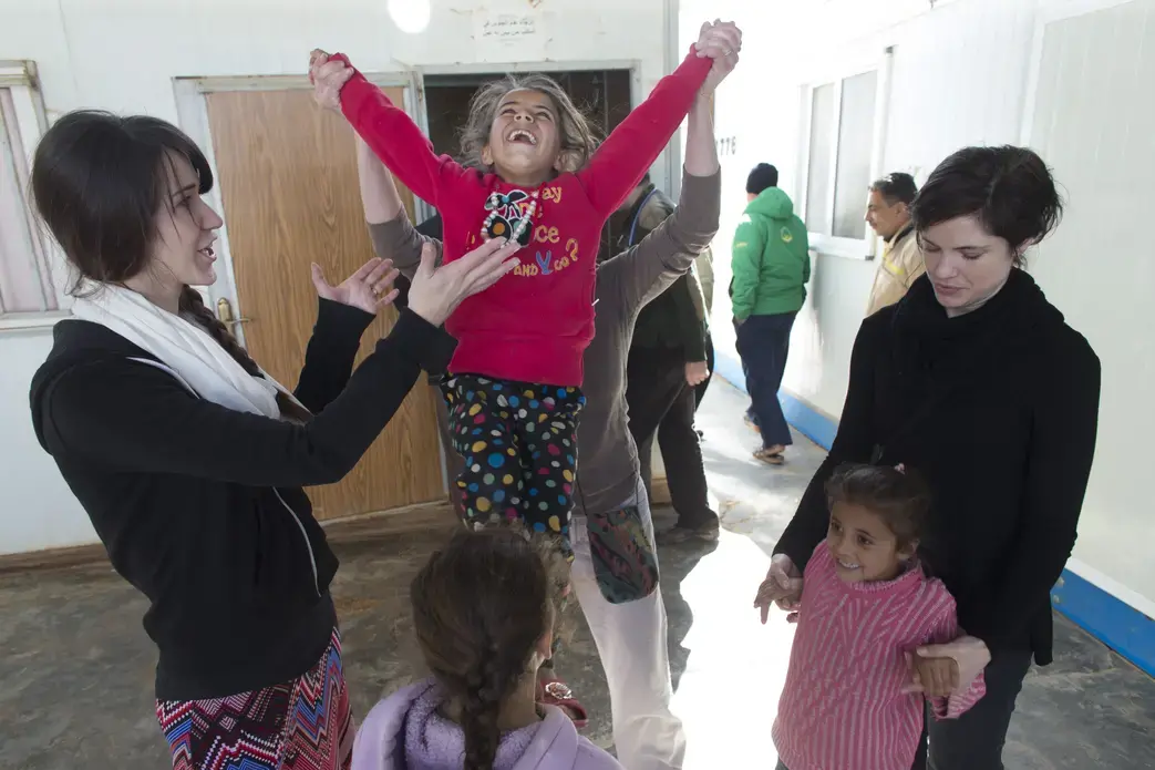 Social worker Stacey Volkman launches a girl into the air while playing with children along with Jennifer Nitschke-Thomas (left) and JoAnna Balza (right) Sunday, March 20, 2016 at the Zaatari refugee camp in Jordan about 15 miles from the Syrian border. Image by Mark Hoffman. Jordan, 2016. Media file: jordan_zaatari_girl_fling.jpg