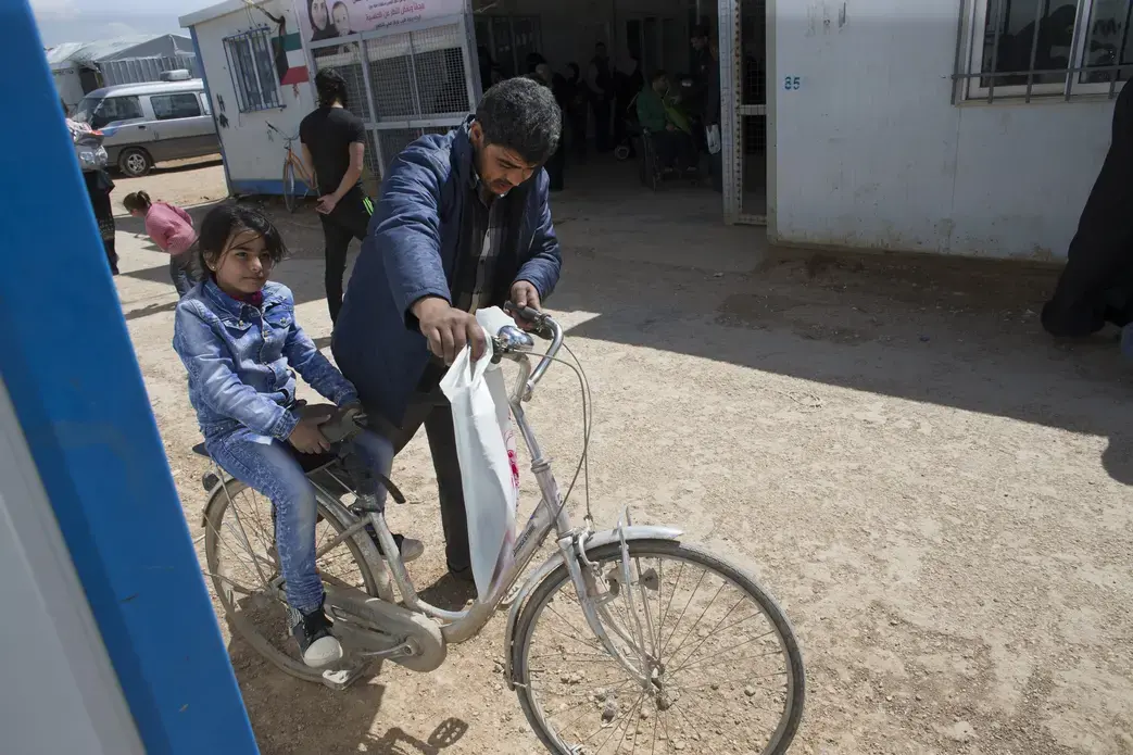 Mahmood Al Mekdad gets on his bike to take his 8-year-old daughter, Sandy, back to their home at the Zaatari refuge camp in Jordan. Image by Mark Hoffman. Jordan, 2016. Media file: jordan5.jpg