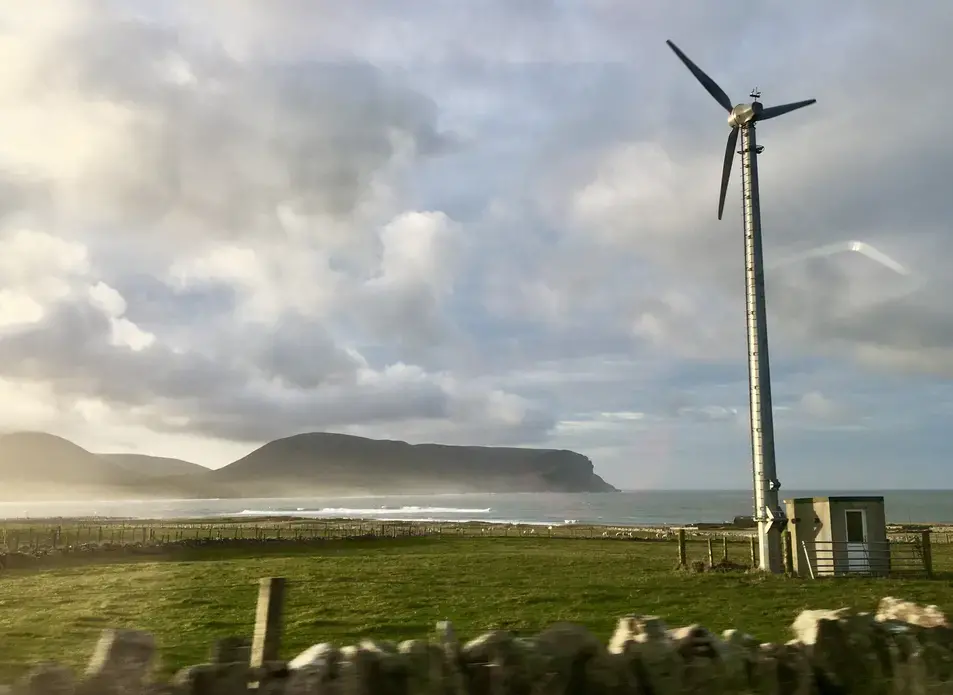 A wind turbine on a farm on the Orkney mainland faces one of the smaller islands off the coast. Image by Maggie More. United Kingdom, 2020. A wind turbine on a farm on the Orkney mainland faces one of the smaller islands off the coast. Image by Maggie More. United Kingdom, 2020.