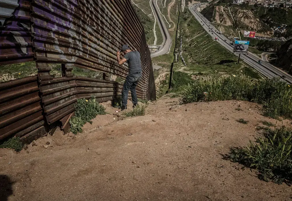  A man, likely a human trafficker known as a 'coyote,' studies a vulnerable stretch of border wall in Tijuana. There is a gap in one area of wall, offering an opening to traffickers of people and drugs. Image by James Whitlow Delano. Mexico, 2017.
