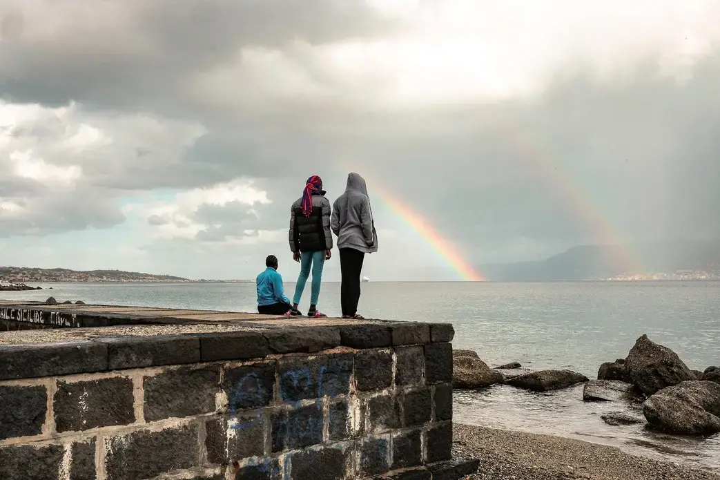 Blessing and two other teen-age Nigerian girls watch a rainbow over the short stretch of water separating Sicily from mainland Italy. Eighty percent of young Nigerian women who cross the Mediterranean are trafficked into sexual exploitation. Image by Ben Taub. Italy, 2017. Blessing and two other teen-age Nigerian girls watch a rainbow over the short stretch of water separating Sicily from mainland Italy. Eighty percent of young Nigerian women who cross the Mediterranean are trafficked into sexual exploitation. Image by Ben Taub. Italy, 2017.