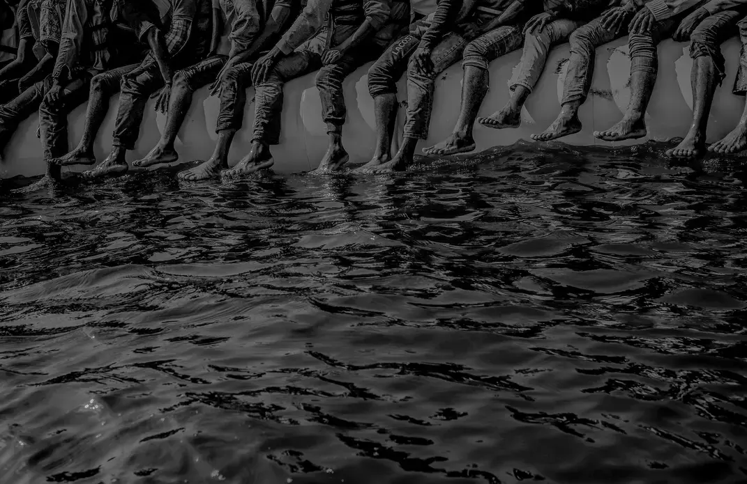 Roughly a hundred and fifty people wait to be rescued from an inflatable dinghy in the Mediterranean Sea, twenty miles north of Libya. The boat left with only enough fuel to reach international waters. Image by Ben Taub. Libya, 2016.