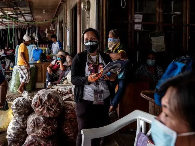 Filipina nurse April Abrias in a crowded vegetable market while checking on patients showing symptoms of Covid-19. Image by Xyza Cruz Bacani. Philippines, 2020. Filipina nurse April Abrias in a crowded vegetable market while checking on patients showing symptoms of Covid-19. Image by Xyza Cruz Bacani. Philippines, 2020.