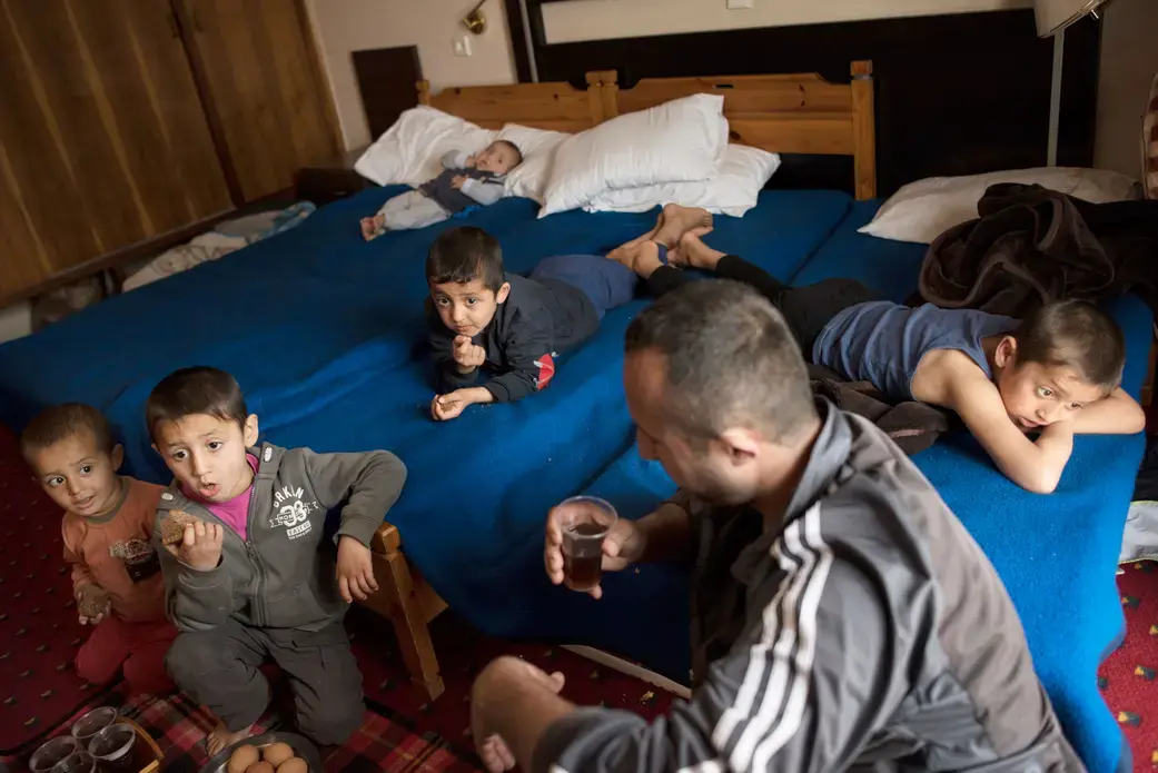 Minhel drinks tea while his children watch television in a hotel in Kastoria, Greece, near the Albanian border. Image by Lynsey Addario. Greece, 2017. Minhel drinks tea while his children watch television in a hotel in Kastoria, Greece, near the Albanian border. Image by Lynsey Addario. Greece, 2017.