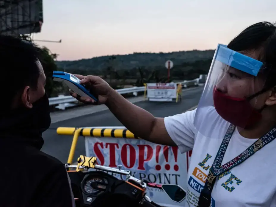 Rose Ann, a rural nurse, checks the temperature of a traveler at a checkpoint. Image by Xyza Bacani. Philippines, 2020. Rose Ann, a rural nurse, checks the temperature of a traveler at a checkpoint. Image by Xyza Bacani. Philippines, 2020.
