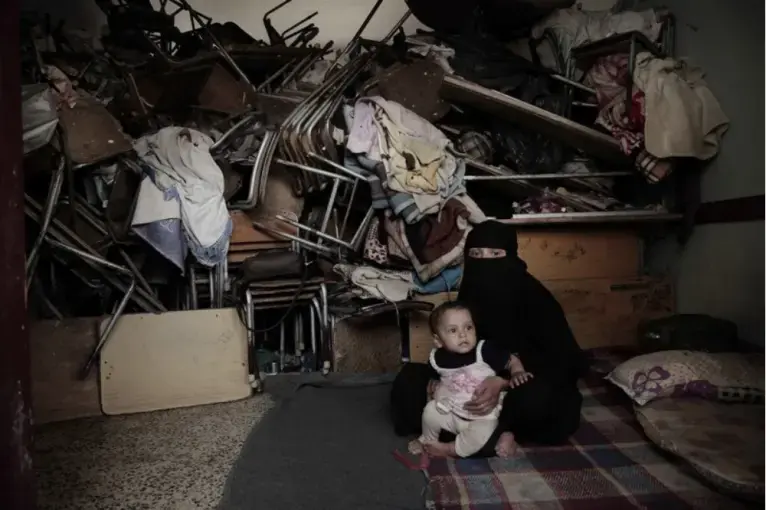 A woman sits with her baby inside a shelter for displaced persons in Ibb. Image by Nariman El-Mofty/AP Photo. Yemen, 2018.