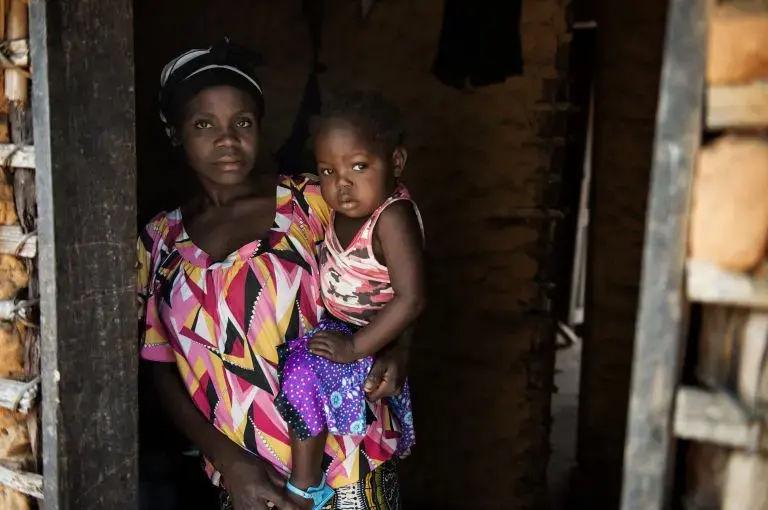 Olga, 30, with her 3 year old daughter Odile in Kahemba. Roughly a year ago Odile stopped moving her legs, Olga is not sure why she became paralyzed but had been feeding her a diet consisting largely of various forms of cassava. Image by Neil Brandvold. DRC, 2016.