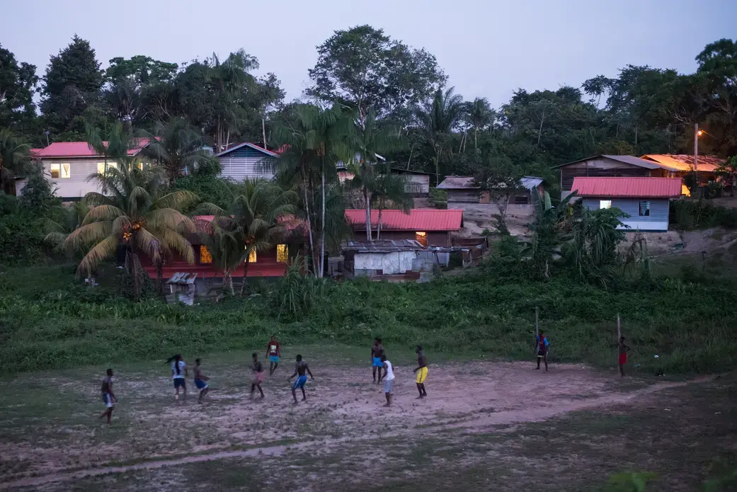 People play soccer as dusk falls on the village of Adjuma Kondre in Suriname. The village's water sources have been impacted by Alcoa's nearby mining operations. Image by Stephanie Strasburg. Suriname, 2017. People play soccer as dusk falls on the village of Adjuma Kondre in Suriname. The village's water sources have been impacted by Alcoa's nearby mining operations. Image by Stephanie Strasburg. Suriname, 2017.