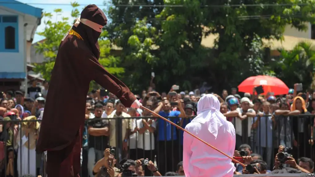 A religious officer canes an Acehnese youth onstage as punishment for dating outside marriage, which is against Sharia, or Islamic law, outside a mosque in Banda Aceh, Aug. 1, 2016. Aceh's landscape is dotted with Saudi influence, but its religious climate is decidedly not. Image from AFP. Indonesia, 2016.