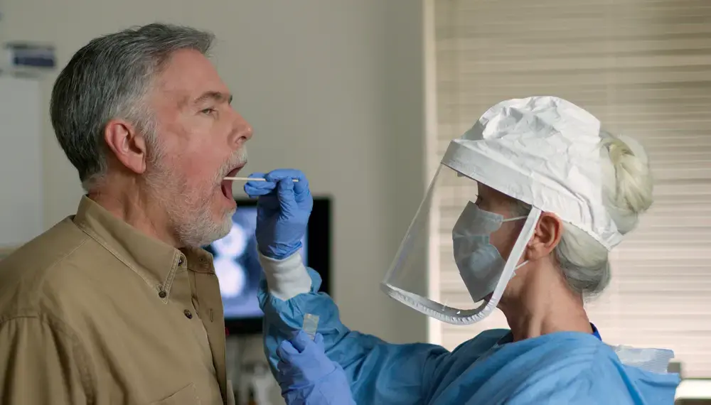 A man being swabbed by a healthcare worker in protective garb to determine if he has contracted the coronavirus. Image by JHDT Productions / Shutterstock. United States, 2020. A man being swabbed by a healthcare worker in protective garb to determine if he has contracted the coronavirus. Image by JHDT Productions / Shutterstock. United States, 2020.