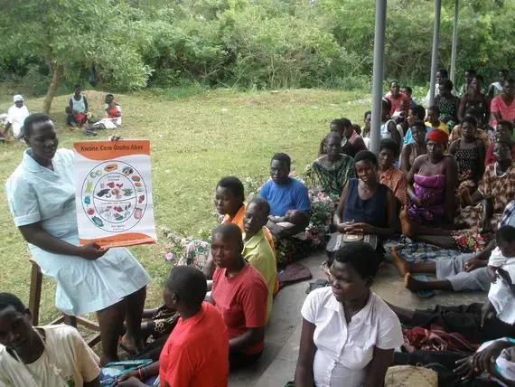 Midwife Susan Ejang explains the importance of good nutrition to a group of pregnant women and new moms gathered on the veranda of a health clinic in northern Uganda. Image by Roger Thurow. Uganda, 2014. Media file: lead.jpg