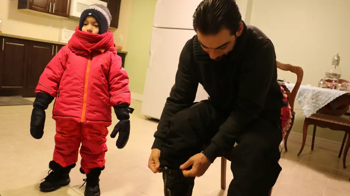 Nagham Al Jabouli, 5, waits for her father to walk her through a snowstorm to her first day of school in Canada. She is wearing snow pants, snow boots, and heavy ski mitts for the first time. Image by Robin Shulman. Canada, 2016. Preparing for a snowstorm