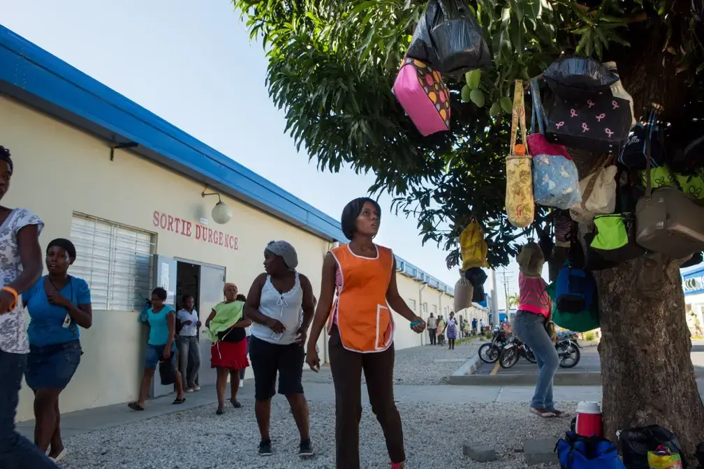 Workers retrieve lunch satchels left hanging in trees outside of a Sae-A Trading Company factory building at the Caracol Industrial Park in the north of Haiti on April 14. Sae-A is the anchor tenant of the $300 million-park, employing about 5,000 workers—still far short of the 60,000 jobs originally projected by 2017. The Clintons were instrumental at nearly every step in its creation. Image by Allison Shelley. Haiti, 2014. Workers retrieve lunch satchels left hanging in trees outside of a Sae-A Trading Company factory building at the Caracol Industrial Park in the north of Haiti on April 14. Sae-A is the anchor tenant of the $300 million-park, employing about 5,000 workers—still far short of the 60,000 jobs originally projected by 2017. The Clintons were instrumental at nearly every step in its creation. Image by Allison Shelley. Haiti, 2014.