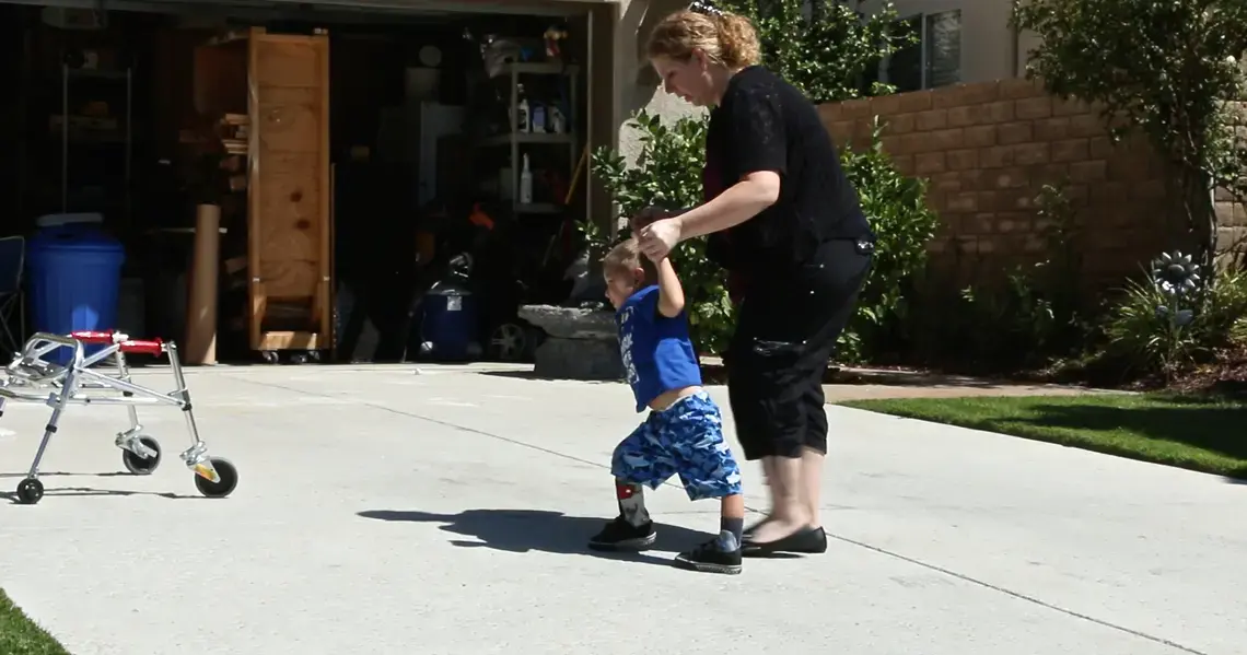 Erin Olivera helps her son Lucian walk up the family driveway. The boy has been diagnosed with a polio-like syndrome that has caused paralysis in both legs. Image by Jake Nicol. United States, 2015. Media file: lucianerin.jpg