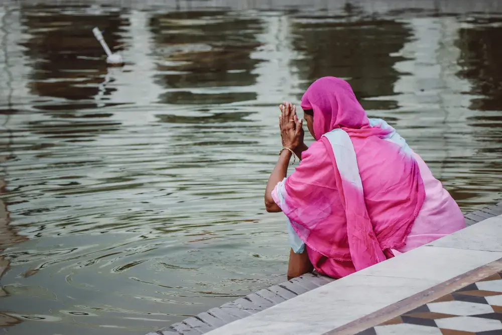 Sikh woman in pink sari dress praying at sacred pool. Image by Gabriela Rosell / Shutterstock. India, undated. Sikh woman in pink sari dress praying at sacred pool. Image by Gabriela Rosell / Shutterstock. India, undated.