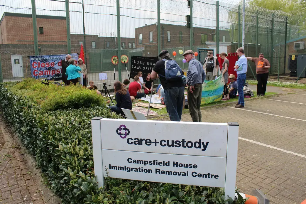 Protestors gather outside the detention center, which is run by Mitie, a private corporation. They object to what they consider exploitative practices by Mitie and the fact that migrants can be detained without judicial oversight. Image by Abe Kenmore. United Kingdom, 2016. Media file: img_0879.jpg