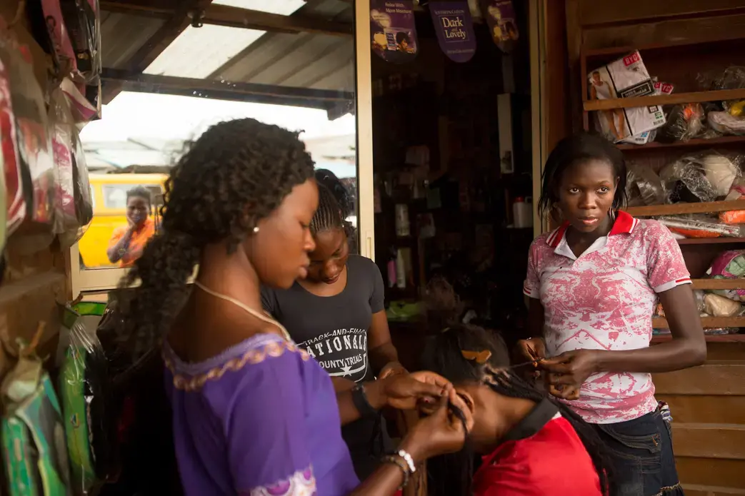 In Lagos, Nigeria, "Morayo" (assumed name), right, 21, braids hair at the salon where she is part of an 18-month-long vocational program. At the end of the program, participants are given equipment of their own so that they might start their own business. Morayo had an abortion several years ago at a local clinic but has not told anyone other than her sister. Image by Allison Shelley. Nigeria, 2013. Media file: pulitzer_globalpost_002.jpg