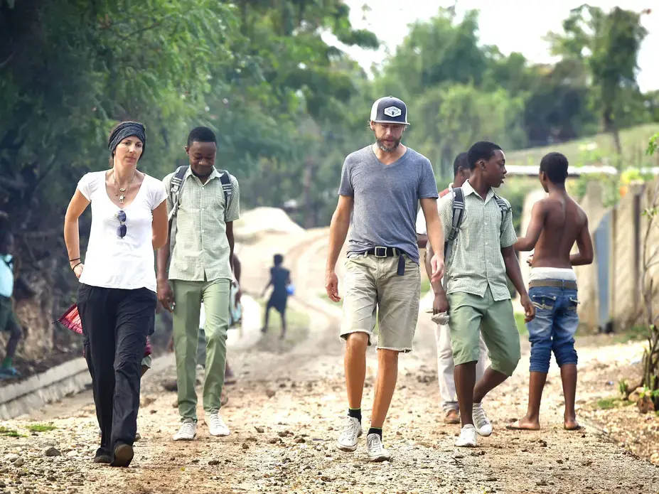 Hands and Feet Project directors Andrea and Will McGinniss walk with older boys on their way to school. The two teenagers behind the McGinnisses have moved into transitional homes from the Hands and Feet children's village in Haiti. Image by Larry McCormack. Haiti, 2016. Media file: haiti_aid.jpg