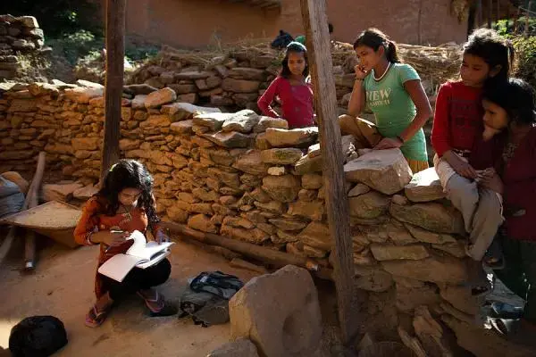 Fourteen-year-old Radhika Sunar, left, studies in the yard in front of her home as friends watch in Siddheshwar village, Achham, Nepal. Girls are banned from certain areas during menstruation, including inside of their homes, forcing them to study, eat, and bathe outdoors. "I don't like it at all," she says. "When I'm walking everyone yells at me 'Don't touch this! Don't touch that!" Image by Allison Shelley. Nepal, 2012. Media file: chaupadi.jpg