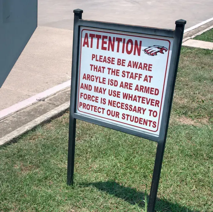 Sign warns that there are armed staff members at Texas school. Image by Spike Johnson. United States, 2018. Sign warns that there are armed staff members at Texas school. Image by Spike Johnson. United States, 2018.