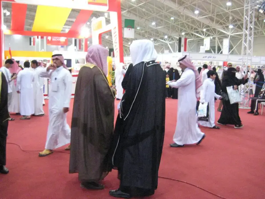 Two religious policemen on patrol at Riyadh's International Book Fair. Although the strict interpretation of Islam prevalent in Saudi Arabia, Wahhabism, frowns upon fancy dress as an impious pretension, the religious police often wear the formal robe, the bisht, as seen here. Image by Caryle Murphy. Riyadh, 2014. Media file: muttawa_or_religious_police_at_the_book_fair.jpg