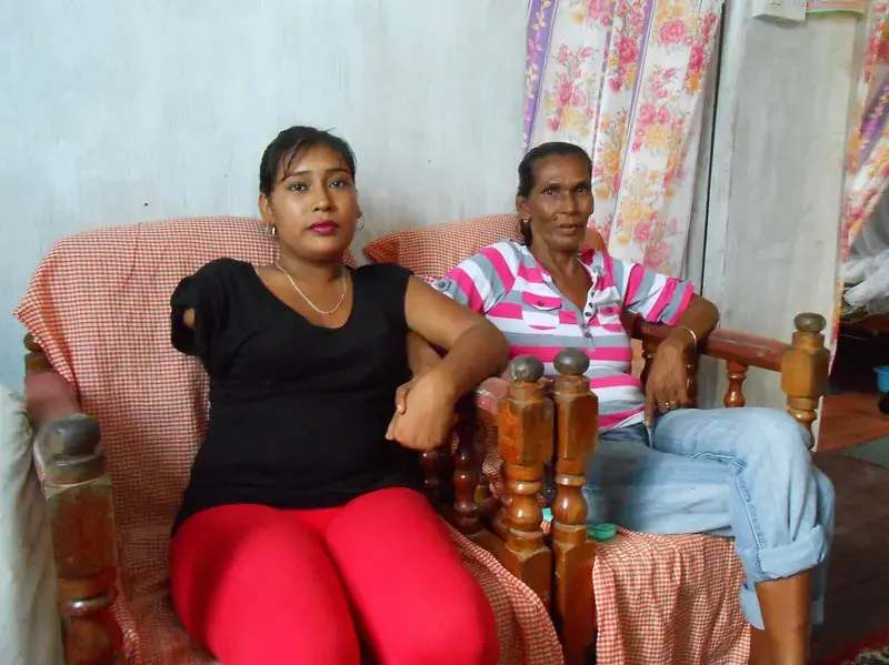 Natasha Houston and her mother at home in Zeelgult. In 2013, Houston's husband killed their two children, slashed her arm and hand, then died, apparently by suicide. Image by William Rawlins. Guyana, 2018. Natasha Houston and her mother at home in Zeelgult. In 2013, Houston's husband killed their two children, slashed her arm and hand, then died, apparently by suicide. Image by William Rawlins. Guyana, 2018.