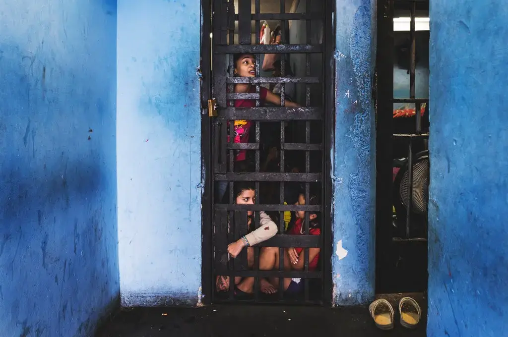 Keylis, 28, top, and Hainni, 17, below left, at La Yaguara Detention Center, Caracas, chat with male prisoners locked up just a few meters away from them. Image by Ana María Arévalo. Venezuela, 2018.