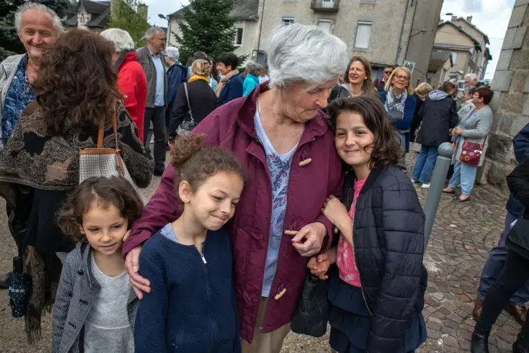 Michelle Baillot brings Touana (5), Schkourtessa (7) and Erlina Sélimi (10) to France’s World War II Victory Day at Le Chambon-sur-Lignon’s town’s square.  The girls are from a Kosovar refugee family that Baillot has been close to now for ten years. “I tell them that you are not from here, so you are going to have to be better than everyone else.” Image by Lucian Perkins. France, 2018.