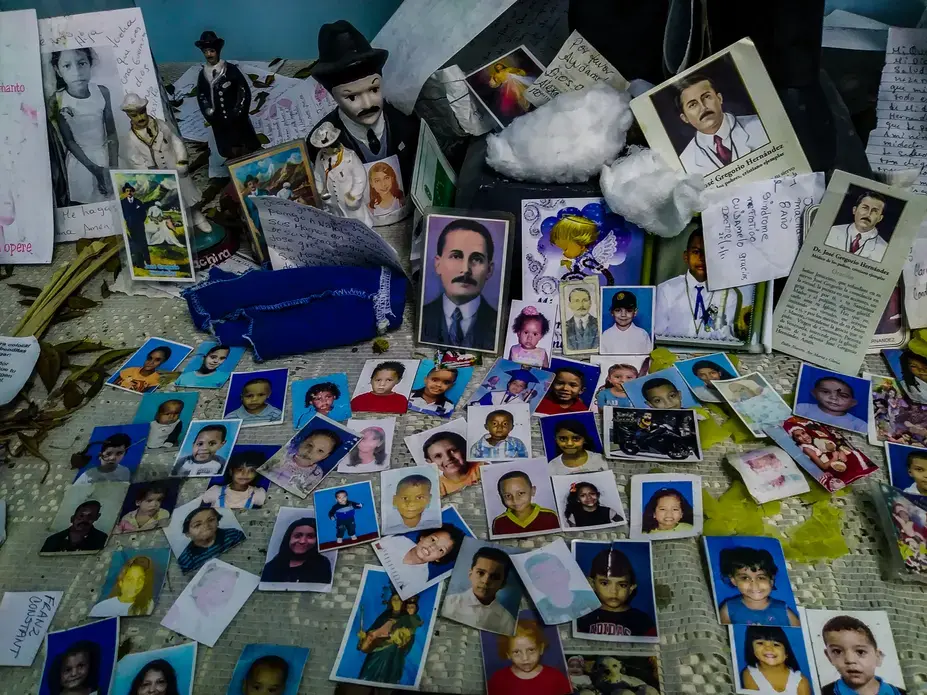 An improvised altar in honor of José Gregorio Hernández at the Hospital J.M de los Ríos. Hernández, a Venezuelan doctor widely known and remembered by his kindness and service to the poor, is considered a saint by many Catholics in Venezuela, who often think of him as the protector of the ill. At the pediatric hospital, mothers and family members put photos of their children at the altar to pray for their good health and swift recovery. Image by Flaviana Sandoval. Venezuela, 2018. An improvised altar in honor of José Gregorio Hernández at the Hospital J.M de los Ríos. Hernández, a Venezuelan doctor widely known and remembered by his kindness and service to the poor, is considered a saint by many Catholics in Venezuela, who often think of him as the protector of the ill. At the pediatric hospital, mothers and family members put photos of their children at the altar to pray for their good health and swift recovery. Image by Flaviana Sandoval. Venezuela, 2018.