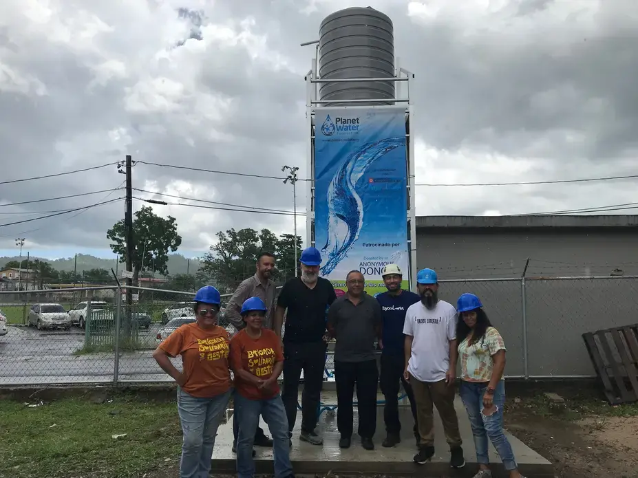 After a whole day of work, members of Brigada Solidaria and Rayo De Luna stand in front of the water tower they installed, which will provide Añasco residents and students of the Escuela Espino elementary school with filtered water. Image by Tomas Woodall Posada. United States, 2018.