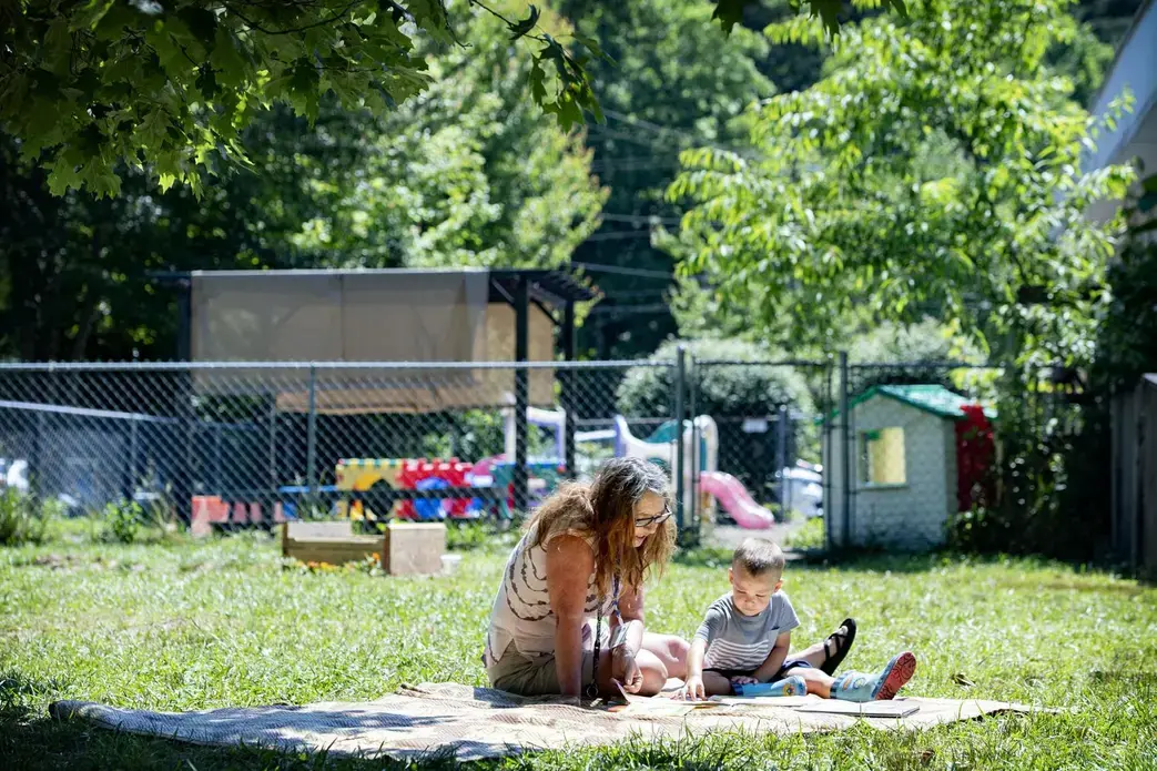 Bell’s School teacher Angela Mehaffey reads a book with Elliot Fink, 2, on a blanket outside the Fletcher preschool June 22. Image by Angeli Wright/Asheville Citizen Times/North Carolina News Collaborative. United States, 2020. Bell’s School teacher Angela Mehaffey reads a book with Elliot Fink, 2, on a blanket outside the Fletcher preschool June 22. Image by Angeli Wright/Asheville Citizen Times/North Carolina News Collaborative. United States, 2020.