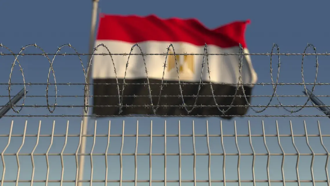 Blurred waving flag of Egypt behind barbed wire fence. Image by Novikov Aleksey. Undated. Blurred waving flag of Egypt behind barbed wire fence. Image by Novikov Aleksey. Undated.