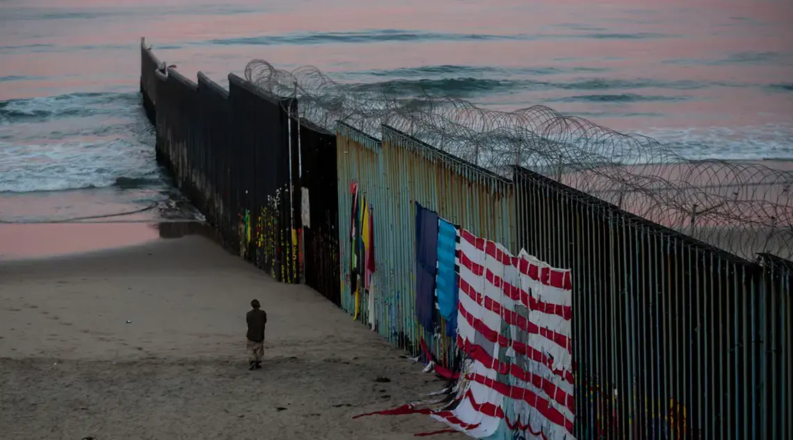 In Tijuana, a man walks at sunrise along the border fence where it meets the Pacific Ocean. Image by Erika Schultz. Mexico, 2019. In Tijuana, a man walks at sunrise along the border fence where it meets the Pacific Ocean. Image by Erika Schultz. Mexico, 2019.