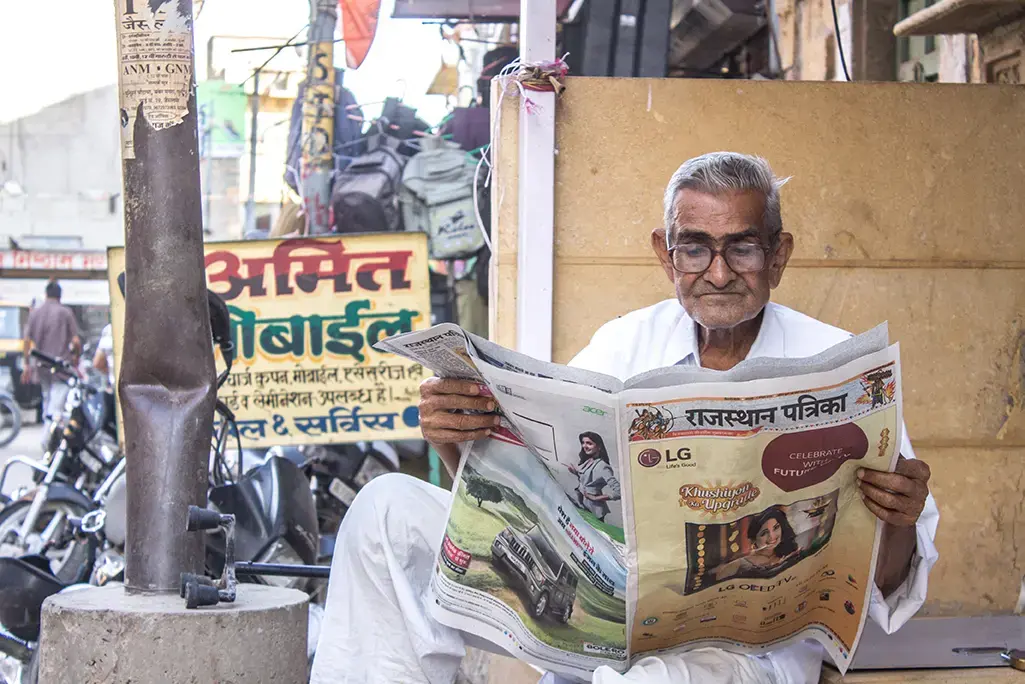 A Rajasthani man reads a local newspaper in the streets outside the Jaisalmer fort. Image by Ihsan Iqbal / Shutterstock.com. India, 2016.