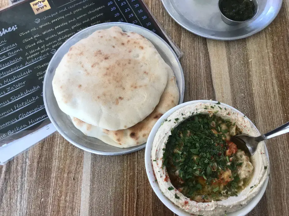 Hummus, pictured here, is more than just a snack. It's considered "worker's food." Historically, it was used to feed those with manual labor jobs who needed a filling breakfast that would get them through an exhausting work day. Today, many hummus establishments continue to exclusively serve the blended mix of tahini, chickpea, olive oil and lemon juice—opening early in the morning and closing once they run out. Image by Carly Graf. East Jerusalem, 2019. Hummus, pictured here, is more than just a snack. It's considered "worker's food." Historically, it was used to feed those with manual labor jobs who needed a filling breakfast that would get them through an exhausting work day. Today, many hummus establishments continue to exclusively serve the blended mix of tahini, chickpea, olive oil and lemon juice—opening early in the morning and closing once they run out. Image by Carly Graf. East Jerusalem, 2019.