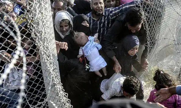Syrian refugees rushing through a hole in the fence near the Turkish border, June 14, 2015. Image by Bulent Kilic/AFP/Getty Images. Syria, 2015. Media file: 477113896_jpg_600x355_q85.jpg