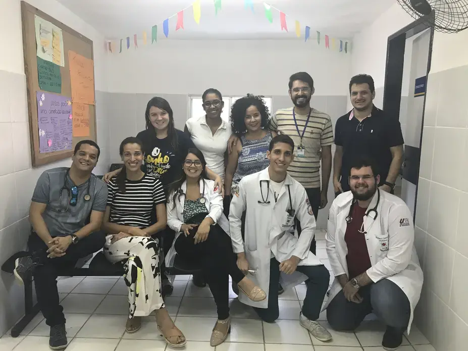 The multidisciplinary healthcare team at the USF in Córrego do Eucalipto. Each USF is supposed to be staffed with a physician, nurse, nurse assistant, and multiple community health agents, in addition to a primary care support team that may include nutritionists, psychologists, social workers, and others. Talita Rodrigues, 26, resident psychologist, is featured in the center in a patterned tank top, with Gerson da Silva, 25, the resident sanitarian, to her immediate right. Image by Poonam Daryani. Brazil, 2017.