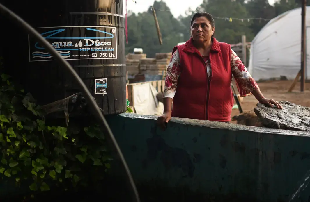 Margarita Reyes takes a break after finishing her typical water gathering routine, which requires her to haul a large pump down to a nearby river. Reyes has lived on the same property her entire life and has watched the Cutzamala System invade her community. She has never had running water in her home despite the proximity of the system. Image by Meg Vatterott. Mexico, 2018. Margarita Reyes takes a break after finishing her typical water gathering routine, which requires her to haul a large pump down to a nearby river. Reyes has lived on the same property her entire life and has watched the Cutzamala System invade her community. She has never had running water in her home despite the proximity of the system. Image by Meg Vatterott. Mexico, 2018.