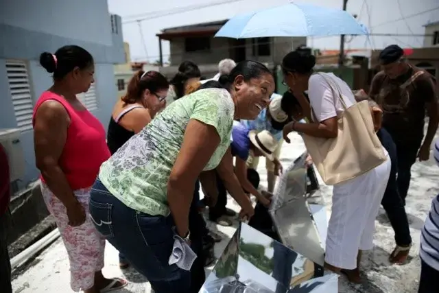 Magdonia Reyes Salazar, a member of the Iglesia Evangelica Dominicana church in Sosua, Dominican Republic, jumps back in surprise after feeling the heat released from a solar oven when opened. The inside of the oven is lined with black material to attract the sun and two plastic lids insulate it. Image by Makenzie Huber. Dominican Republic, 2016. Magdonia Reyes Salazar, a member of the Iglesia Evangelica Dominicana church in Sosua, Dominican Republic