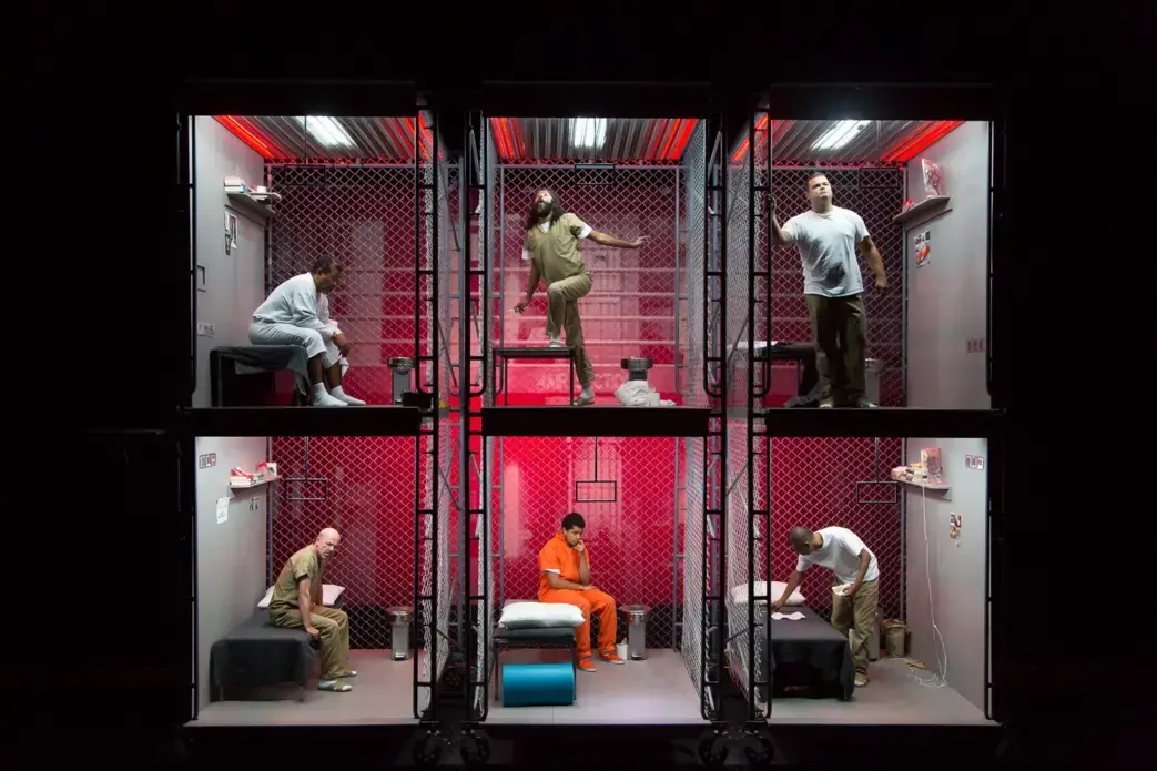 Actors in a multi-level prison cell set on stage during a performance of The BOX.