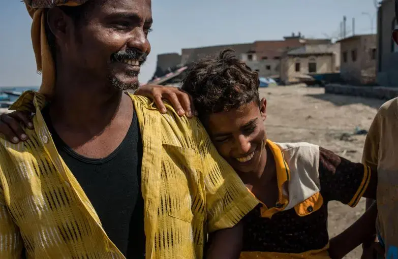 Shafai Saleh Hadi (left) laughs with local boys on the shore of Bir Fuqum. As a first-generation fisherman, he sees the job as a better route for his sons than attending school, since employment is incredibly scarce in Yemen. Image by Alex Potter. Yemen, 2018. Shafai Saleh Hadi (left) laughs with local boys on the shore of Bir Fuqum. As a first-generation fisherman, he sees the job as a better route for his sons than attending school, since employment is incredibly scarce in Yemen. Image by Alex Potter. Yemen, 2018.